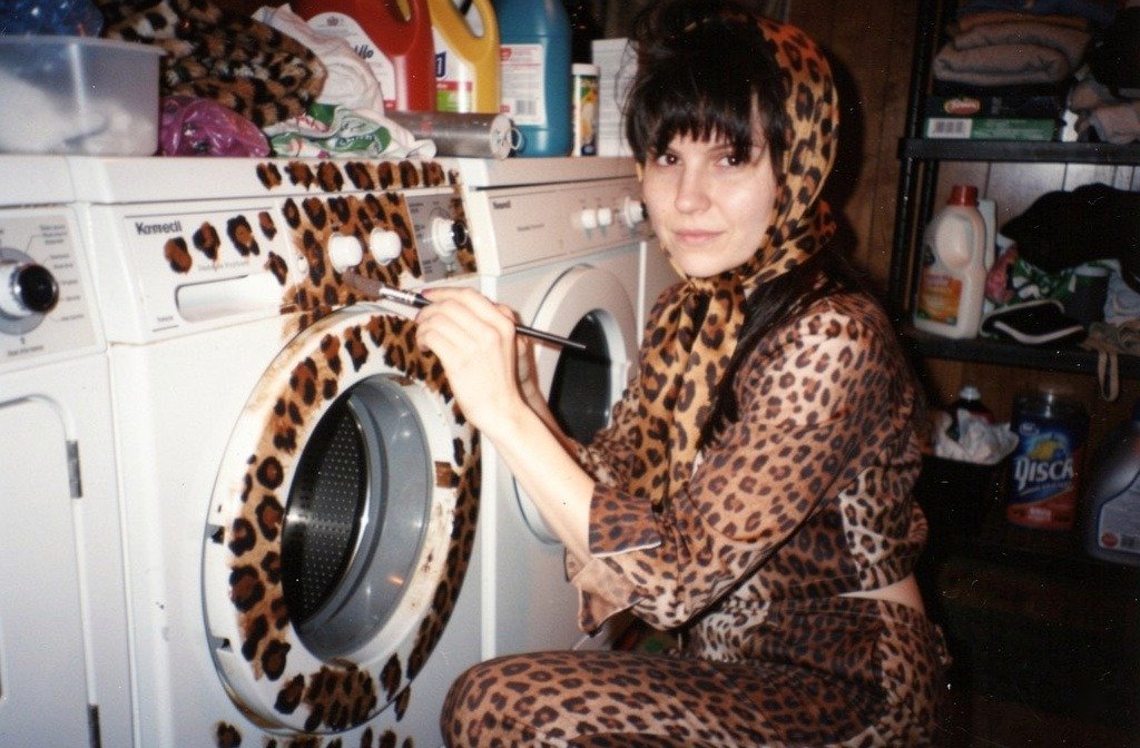 A woman in a leopard-print outfit painting matching spots on a washing machine