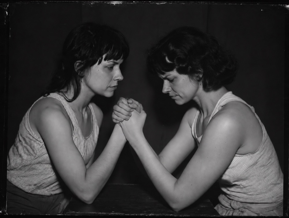 Two identical women arm wrestling across a table